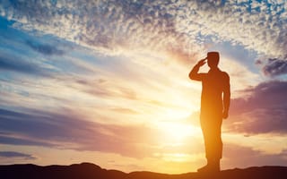 A soldier solutes in front of a sunset.