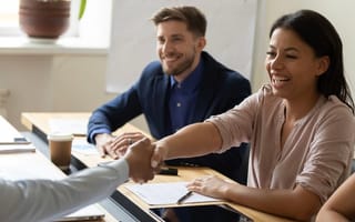 A Black woman smiles and shakes hands with someone across the table