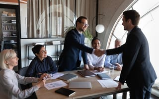 a group of people welcoming another person to an office, with two of them shaking hands