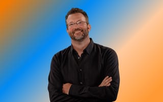 John Linden, co-founder and CEO of Mythical Games, poses for a photo in front of an orange and blue background