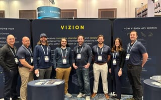 Eight of Vizion's team members posing for a photo in front of a black board with their name on top.