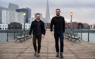 Two Boxes was co-founded by CEO Kyle Bertin (left) and CPO Evan Stalter (right). The two are pictured walking down a wooden pier with buildings in the background.