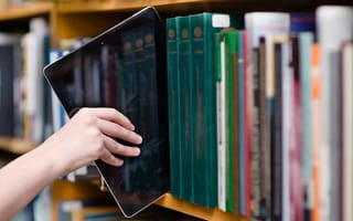 A student pulling a tablet from a bookshelf.