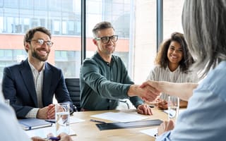 A businessman and businesswoman shaking hands at a group meeting.