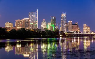 Downtown Austin, Texas at night with lights from skyscrapers reflecting on the near lake.