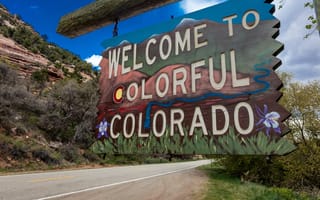 A Welcome to Colorado road sign with mountain landscape behind it.