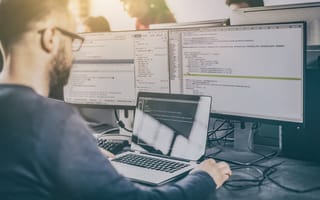 A developer writes code on a computer with multiple screens.