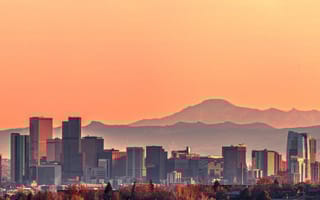 A photo of the Denver skyline, with mountains in the background, against an orange sky.
