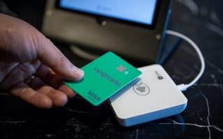 A hand holding an Upgrade-branded Visa card over a touch payment machine, as if making a purchase.