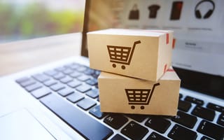 Two parcels with shopping cart icons on them sit atop a laptop.