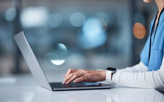 A healthcare professional types on a laptop.