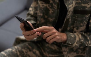 A person in army fatigues holding a cellphone.