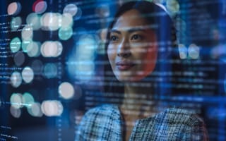 An Asian female stands looking confident and inspired as she studies lines of code on a screen before her eyes