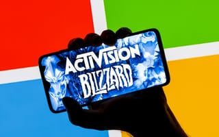 ctivision Blizzard logo on smartphone screen in hand against background of Microsoft logo.