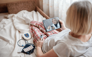 Old woman in bed looking at screen of laptop and consulting with a doctor online at home