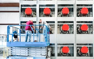 Some workers stand on a hydraulic lift in front of a data center..