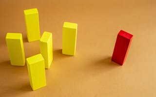 A red wooden block stands apart from a group of yellow wooden blocks, illustrating the marginalization that microaggressions cause in the workplace.