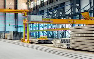 Cement manufacturing floor with pallets of cement bricks piled up and yellow cross-beams going across the space.