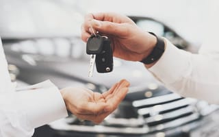 A person is depicted handing car keys to someone in a dealership.