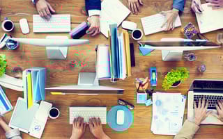 Birds-eye view of Group of Business People Working on an Office Desk. Only their hands are visible as they work at computers.