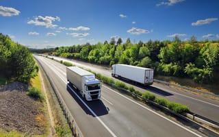 Two semi-trucks are shown driving in opposite directions on the highway.