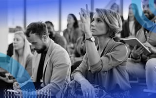 A woman sitting with a group of people is raising her hand to ask a question.