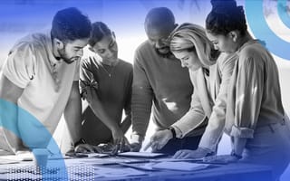A group of happy and diverse employees are collaborating as they stand at a table.