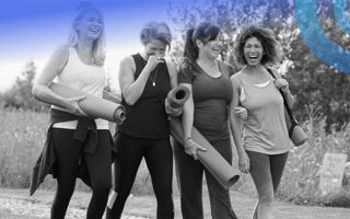 Four women are carrying yoga mats and laughing and talking.