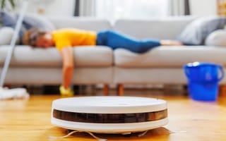 photo of a vacuum cleaning robot in the foreground and an exhausted house cleaner in the background