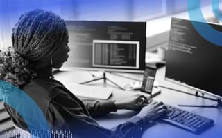 A woman from the waist up coding on a computer with two screens.