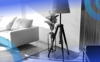 A standing lamp in a living room next to a potteed plant and sofa.