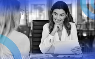 A woman is smiling and looking at a sheet of paper, and another woman sits across from her.