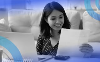 A smiling woman is looking at a paper pay stub.