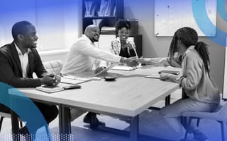 Two people are shaking hands at a conference table as two other people look on.