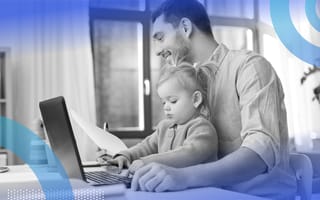 A man holding a baby is working from home with a laptop.