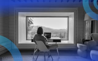 A woman is sitting at a desk that overlooks a calm mountain view.