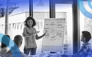 A smiling woman leading a meeting, pointing at a large chart while three colleagues watch and listen.