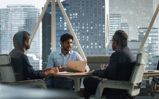 Three men talk around a table in an office.