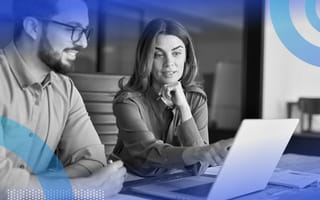 Two coworkers are sitting at a desk and looking at a piece of paper.