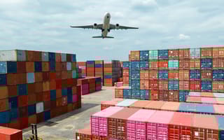The illustration shows an airplane flying over a freight yard filled with shipping containers.