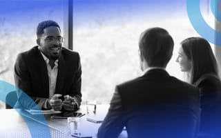 Three people are seated at a table. One is making a presentation to the other two.