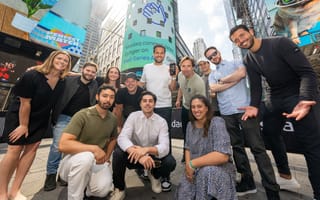 Gynger team members smiling and posing for group photo in front of the Nasdaq stock exchange building display in Times Square in NYC, celebrating their Series A funding round.