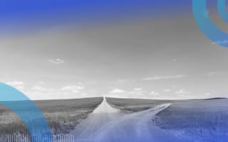 A dirt road the splits into two paths, surrounded by grass on either side with a clear sky above.