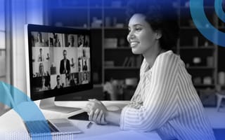 A smiling woman sitting at a desk with a laptop and large computer monitor in front of her.