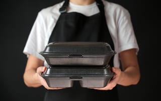 Restaurant worker wearing black apron holding packaged food, ready for delivery.