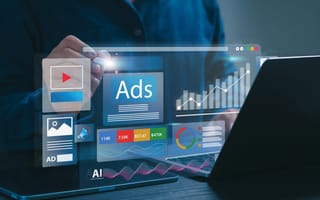 A digital illustration featuring the word "Ads" next to a bar graph and media icon for a video player hovers over a laptop keyboard to represent advertising technology.