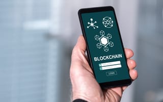 A close-up image of a hand holding a mobile phone with an illustration on the screen that features the world "Blockchain."