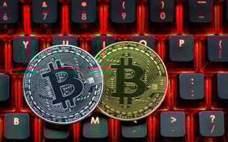 Two coins — one gold and the other silver — featuring the Bitcoin unicode symbol sit on top of a computer keyboard to represent cryptocurrency.