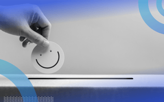 A close-up of a hand dropping a paper smiley face into a feedback bin.
