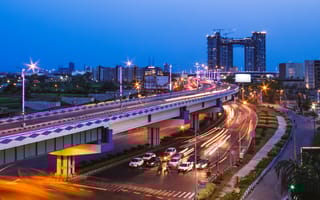 Cars zoom on Kolkata streets and highways at dusk with high-rises in the background.